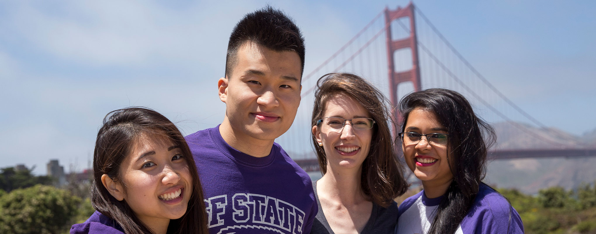Four students wearing SF State purple shirts in front of the Golden Gate Bridge