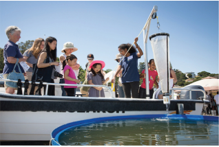 student pulling something out of the water and showing a crowd of spectators